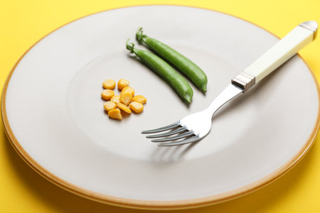 Plate with peas, corn and fork on color background. Concept of anorexiaの写真素材