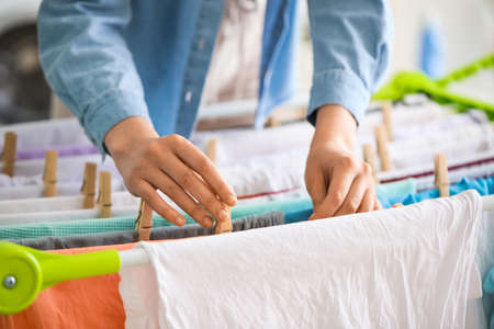 Woman hanging clean clothes on dryer in laundry room, closeup