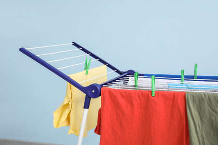 Clean clothes hanging on dryer against color background