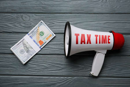 Megaphone with money on gray wooden background. Concept of taxesの写真素材