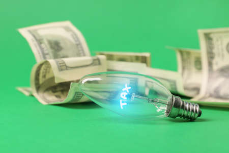 Light bulb with glowing word TAX and dollar banknotes on color background