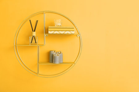 Modern shelf with books and stylish decor hanging on yellow wall in roomの写真素材
