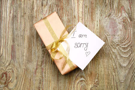 Gift with text I AM SORRY on wooden background