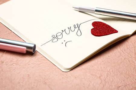 Notebook with written word SORRY on color background