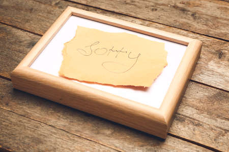 Photo frame and paper sheet with word SORRY on wooden backgroundの写真素材