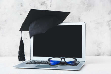 Graduation hat, laptop and glasses on tableの写真素材