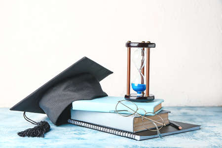 Graduation hat, books and hourglass on tableの写真素材