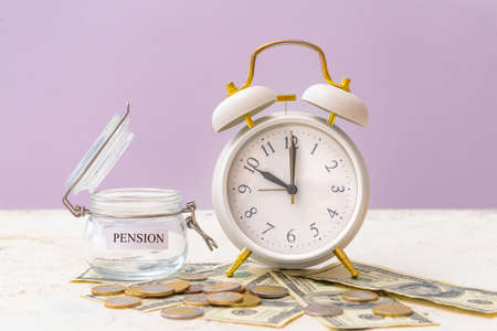 Alarm clock and jar with savings on table. Concept of pension