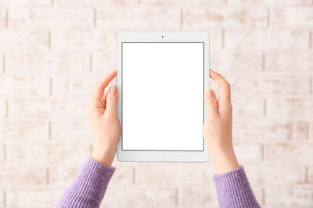 Hands with modern tablet computer on brick background
