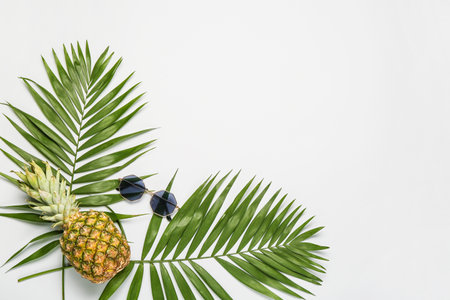 Stylish sunglasses with pineapple and palm leaves on white backgroundの写真素材