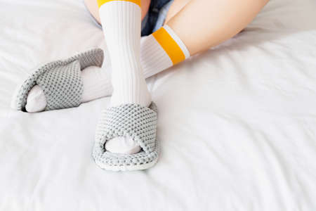 Woman in soft slippers sitting on bed