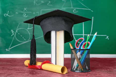 Graduation hat, diploma and stationery on table in classroom
