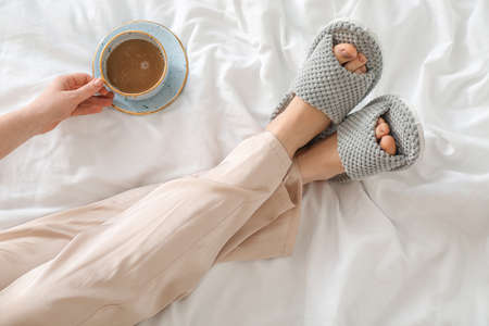 Woman in soft slippers drinking coffee in bedroomの写真素材