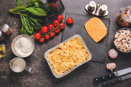 Baking dish with boiled pasta and ingredients on tableの写真素材