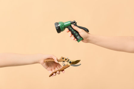 Female hands with water hose and pruner for gardening on color backgroundの写真素材