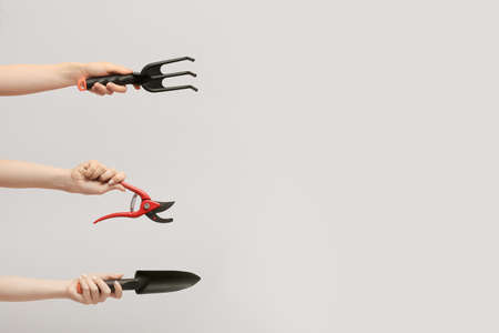 Female hands with gardening tools on light backgroundの写真素材