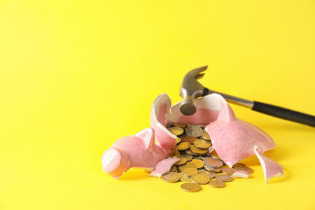 Broken piggy bank, coins and hammer on color backgroundの写真素材
