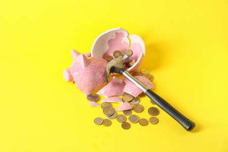 Broken piggy bank, coins and hammer on color backgroundの写真素材