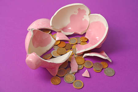 Broken piggy bank and coins on color background