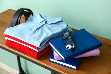 Stylish school uniform with books and eyeglasses on table near color wallの写真素材