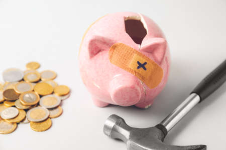 Broken patched piggy bank, hammer and money on light backgroundの写真素材