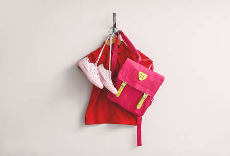 Stylish school uniform with backpack hanging on light wall