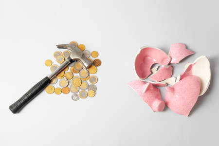 Broken piggy bank, coins and hammer on light backgroundの写真素材