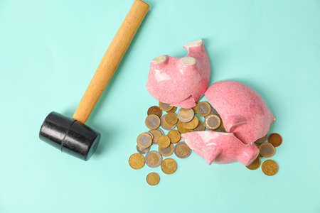 Broken piggy bank, coins and hammer on color backgroundの写真素材