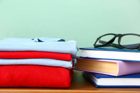 Stylish school uniform with books and eyeglasses on table near color wall