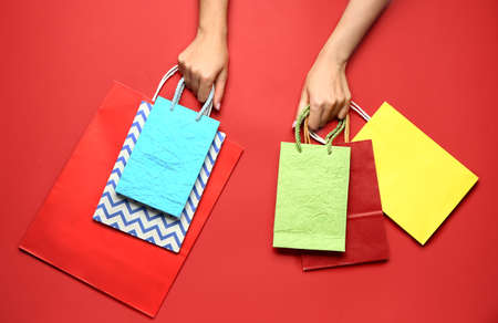 Female hands with paper shopping bags on color backgroundの写真素材