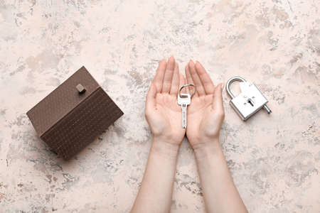 Female hands with key, model of house and padlock on light backgroundの写真素材