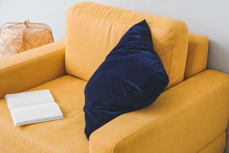 Stylish armchair with pillow and book in room