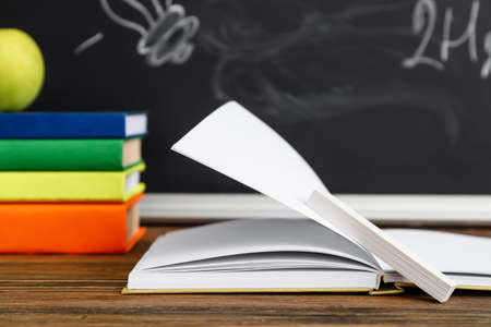 Books and apple on table against school blackboard