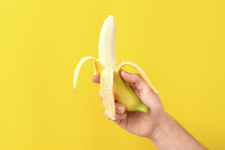 Male hand with ripe banana on color backgroundの写真素材