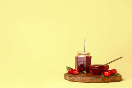 Jar and bowl of tasty strawberry jam on color backgroundの写真素材