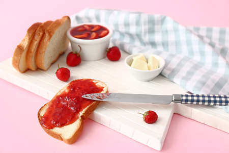 Board with tasty strawberry jam, bread and butter on color backgroundの写真素材