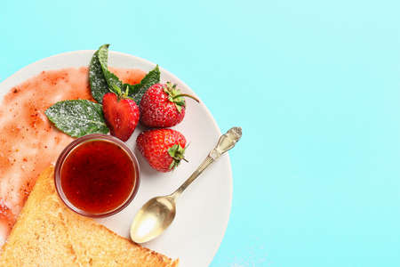 Plate with tasty strawberry jam and bread on color background