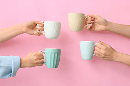 Hands with cups of hot coffee on color backgroundの写真素材