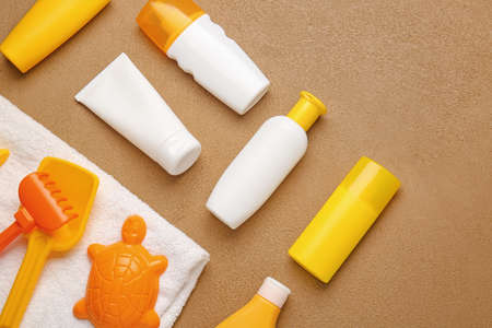 Sunscreen cream with beach sand toys and towel on color background