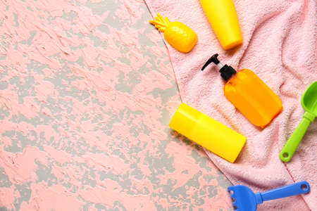 Sunscreen cream with beach sand toys and towel on color background