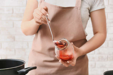 Woman making sweet strawberry jam in kitchen