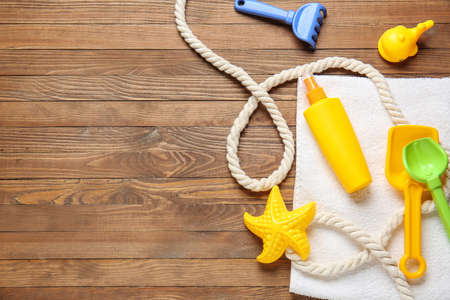 Sunscreen cream with beach sand toys and towel on wooden background