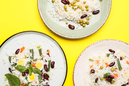 Plates with tasty rice, beans and vegetables on color background