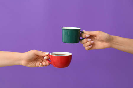 Hands with cups of hot coffee on color backgroundの写真素材