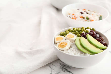 Bowl with tasty rice, beans, avocado and egg on table