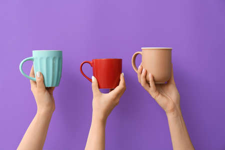 Hands with cups of hot coffee on color backgroundの写真素材