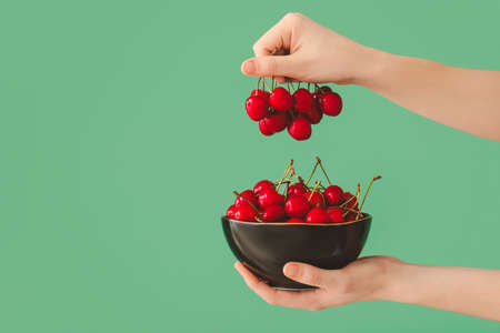Woman with bowl of sweet cherry on color background