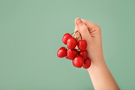 Female hand with sweet cherry on color backgroundの写真素材