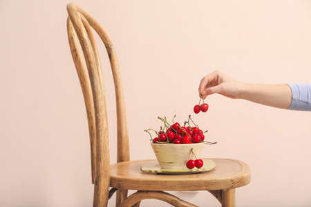 Woman eating sweet cherry from bowl on chair
