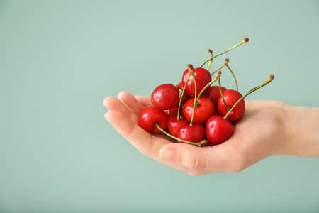 Female hand with sweet cherry on color backgroundの写真素材